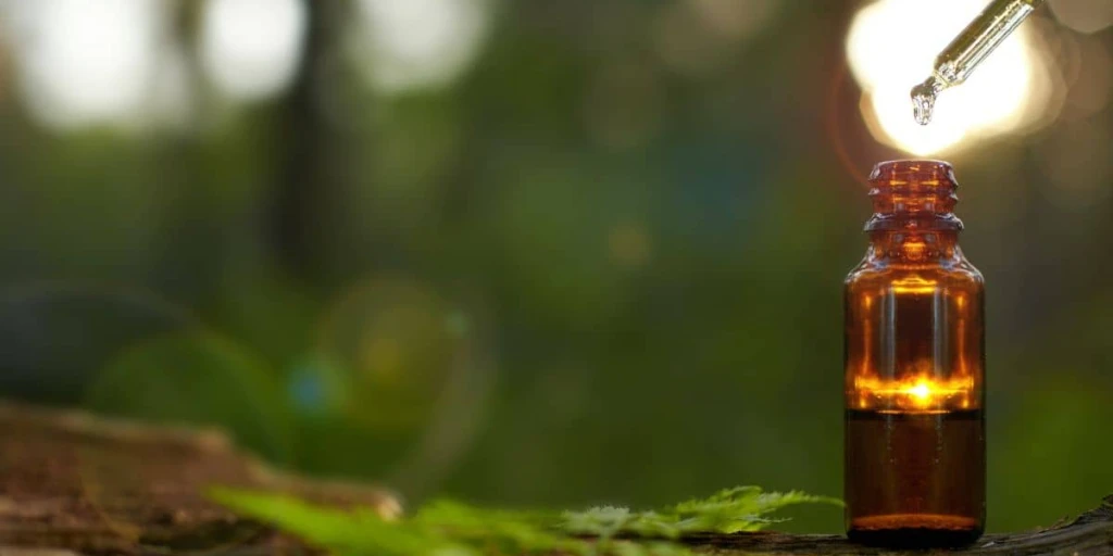 Apothekenfläschchen braun mit Pipette und Tropfen auf Baumstamm, als Sinnbild für Hausmittel
